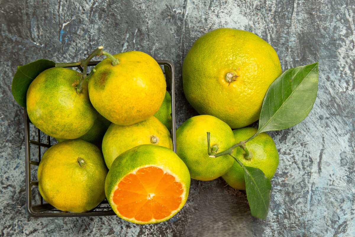 Top view of a basket with fresh green tangerines cut in half and peeled tangerine on the right side of gray background