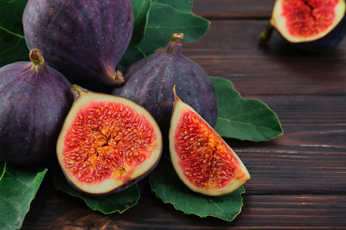 Figs and halves of several fruits close-up on the leaves of a fig tree on an old wooden table, horizontal frame. Seasonal fruits, fig harvest background or mediterranean diet articles